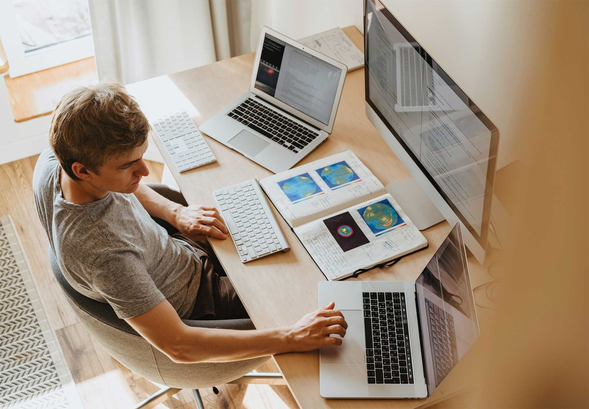 person sitting at desk with two laptops and monitor