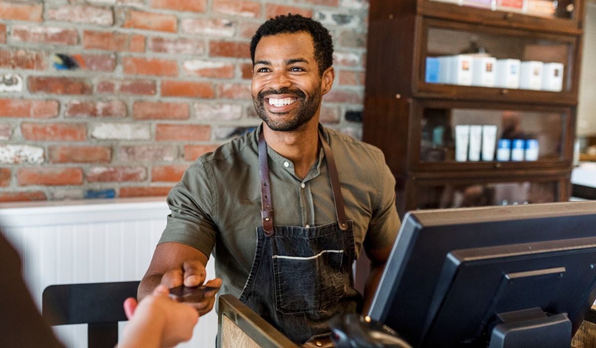 smiling male shop owner handing credit card back to customer